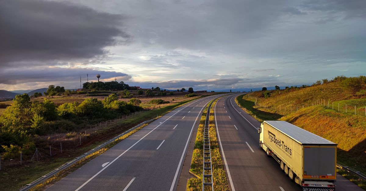 A scenic highway under a dramatic cloudy sky with a lone truck driving on an open road.